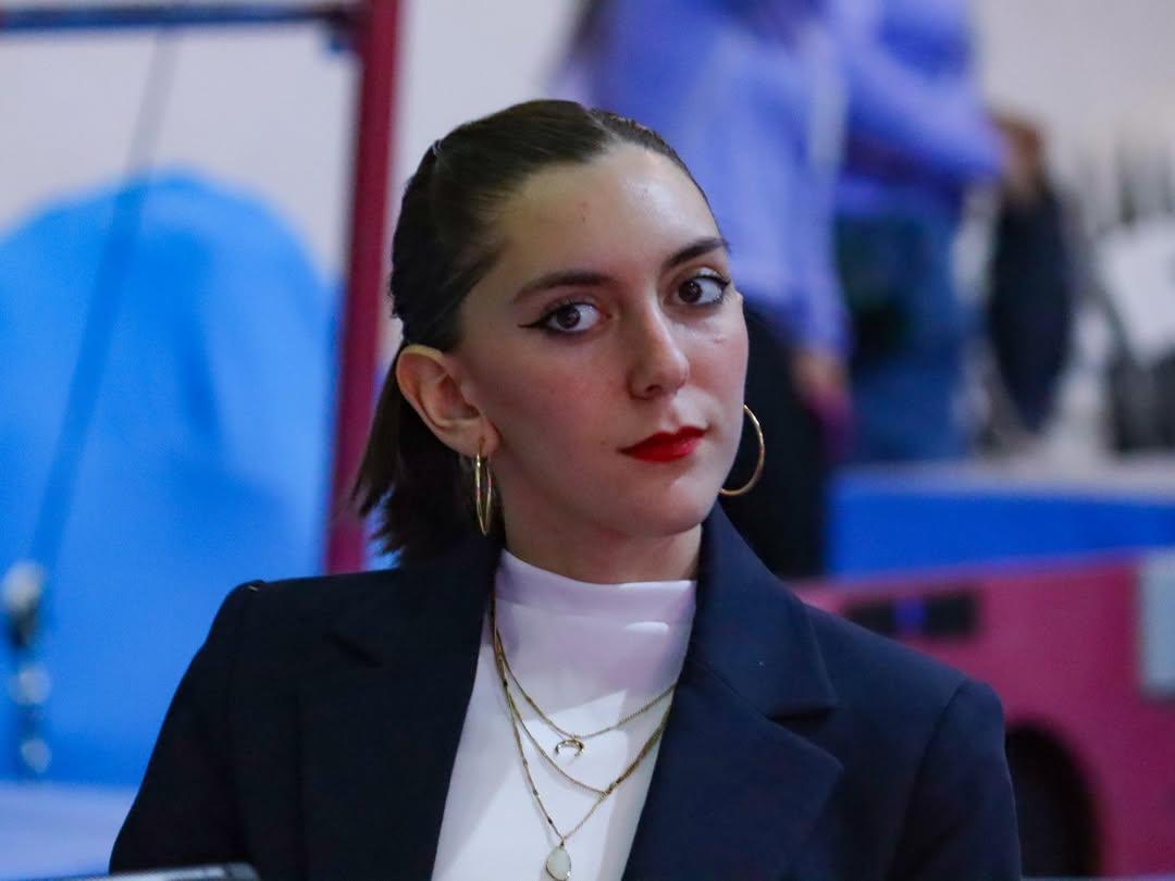 Daniela del Río con saco formal en la mesa de jueces de una competencia de gimnasia