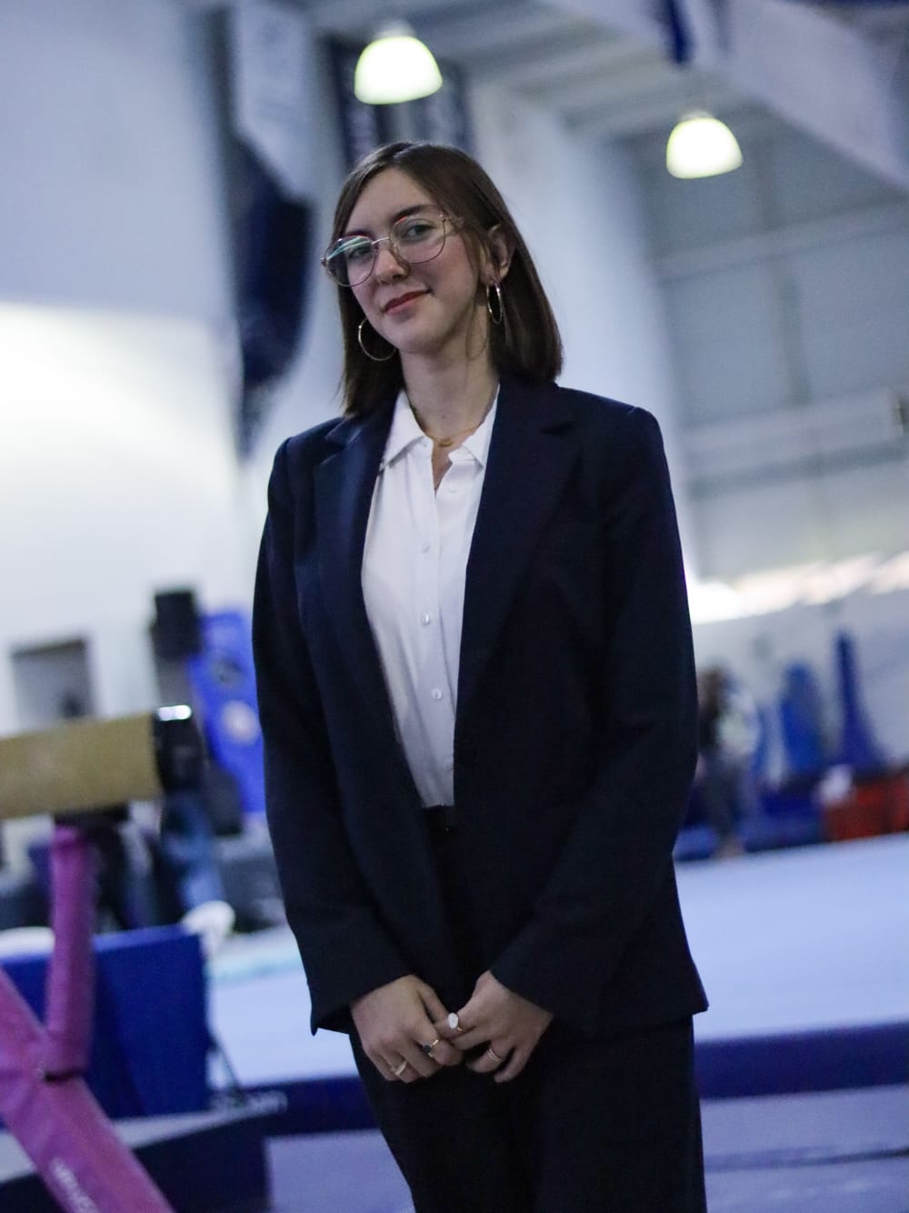 Daniela del Río de pie con traje formal de juez en un gimnasio de gimnasia artística